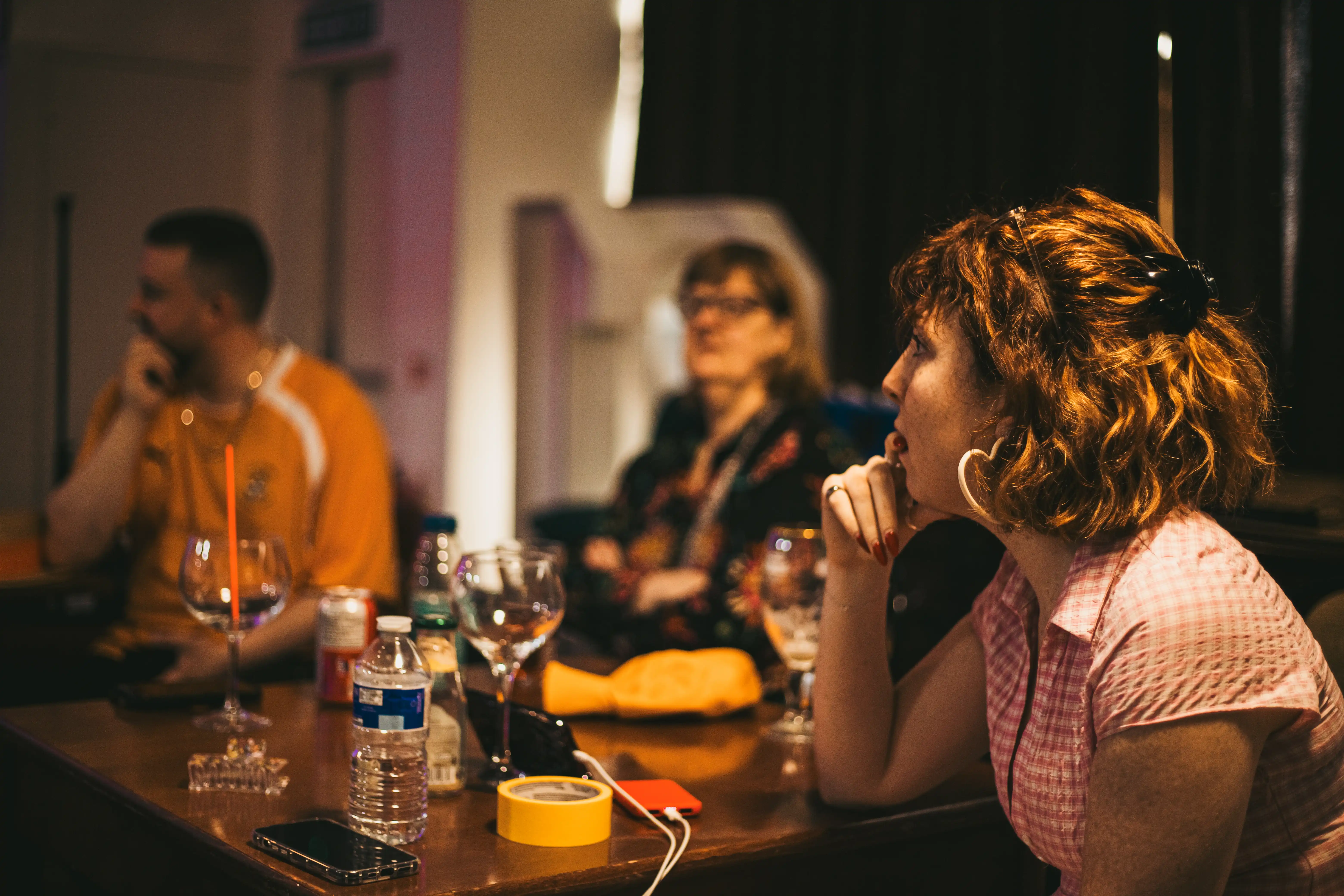 Three people sitting around a table, one man two women. There are several wine glasses and a bottle of water on the table.
