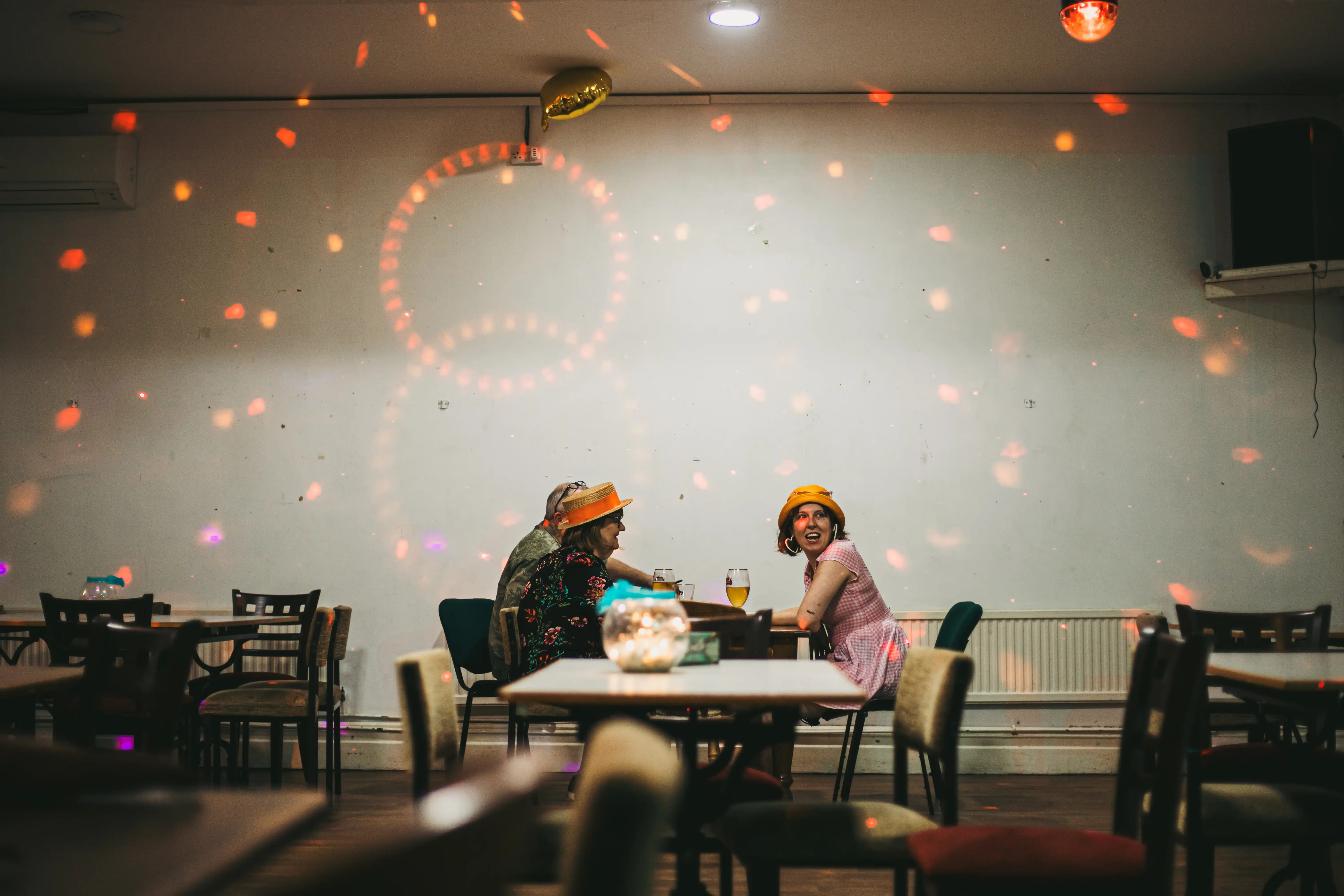 Two people sitting at a table in the distance, surrounded by multiple empty tables and sparkly mood lighting shining on the walls.