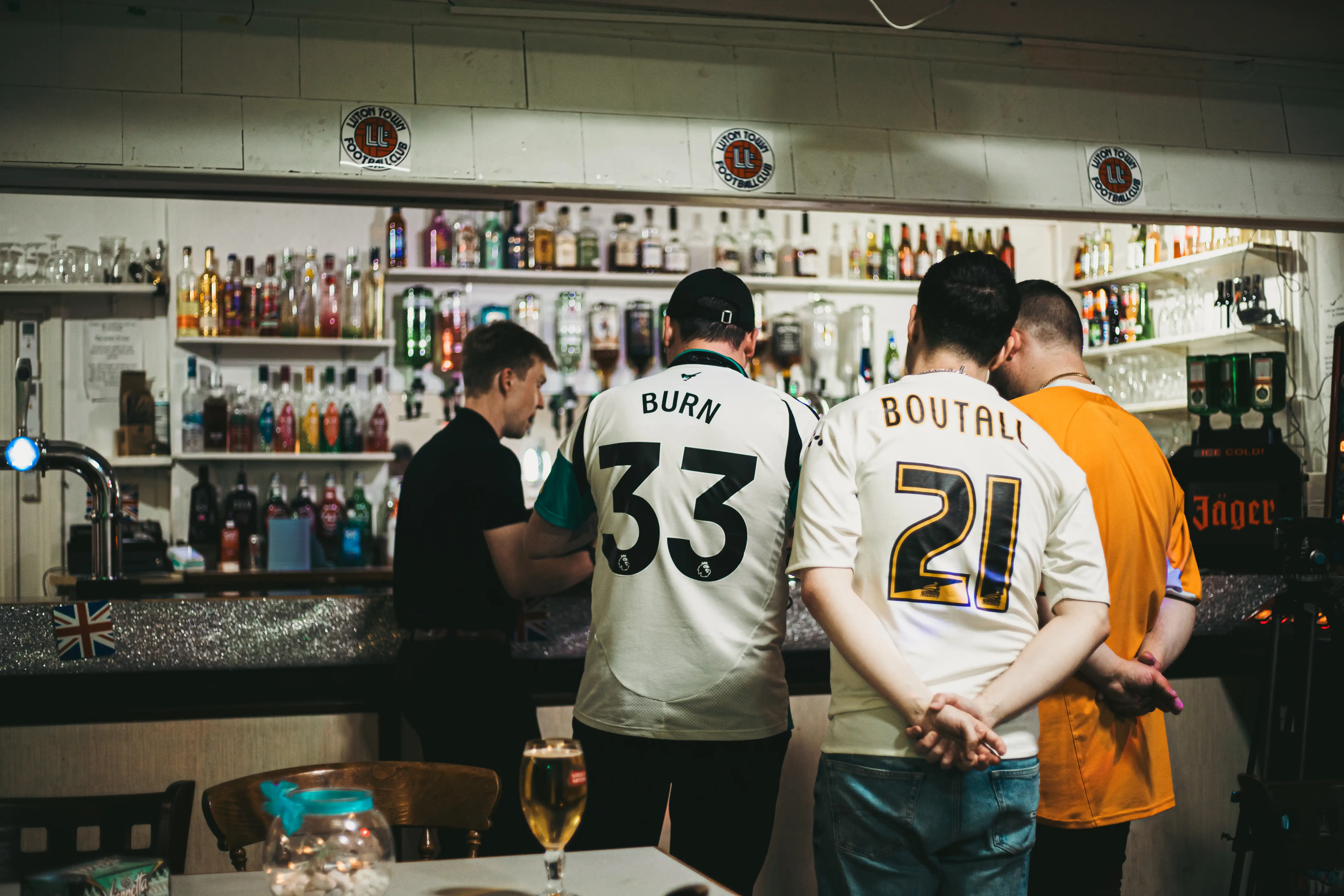 Four men standing in a small circle all looking at something. They are standing at a bar.