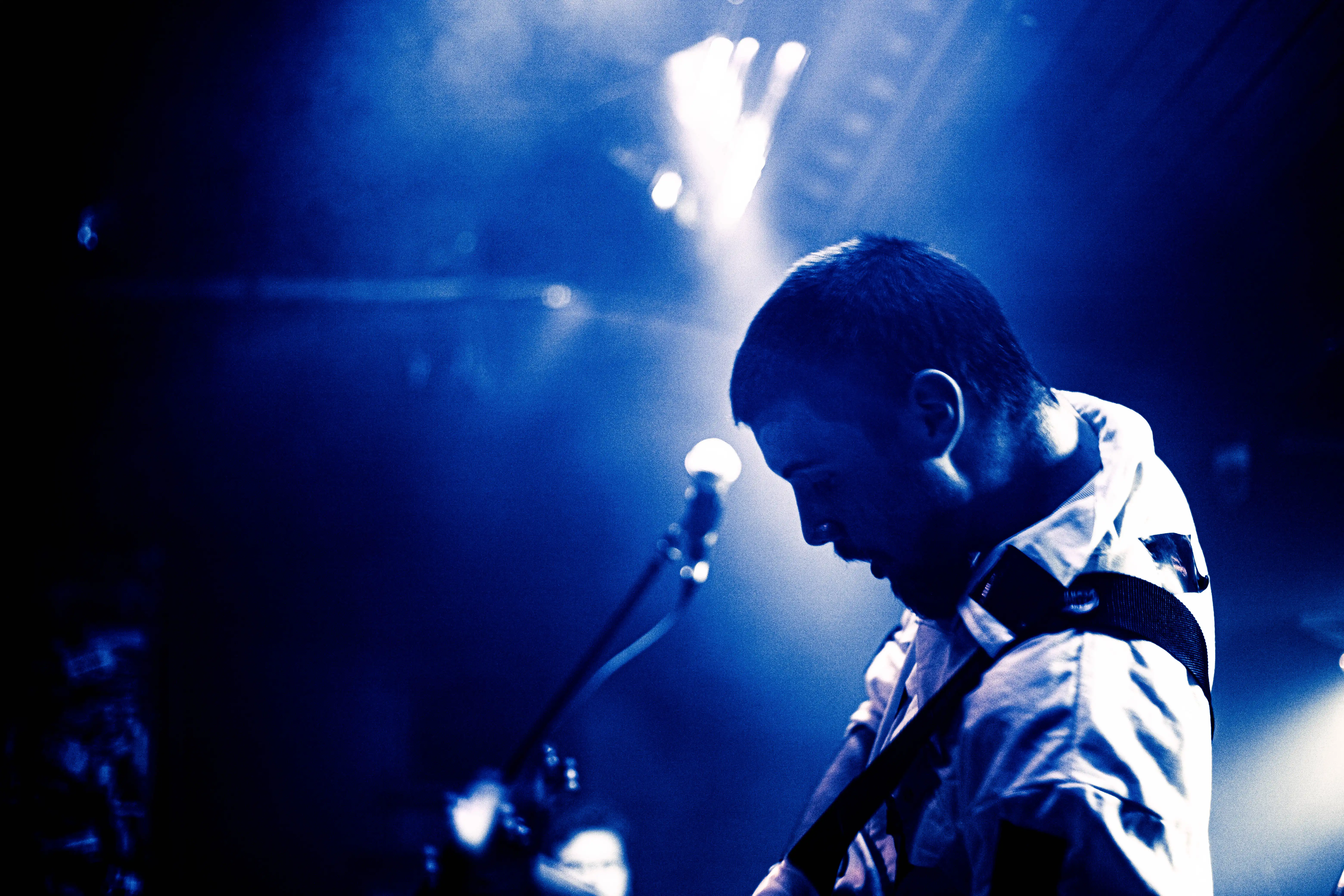 A vivid blue image of a musician playing bass on stage with bright lights in the background.