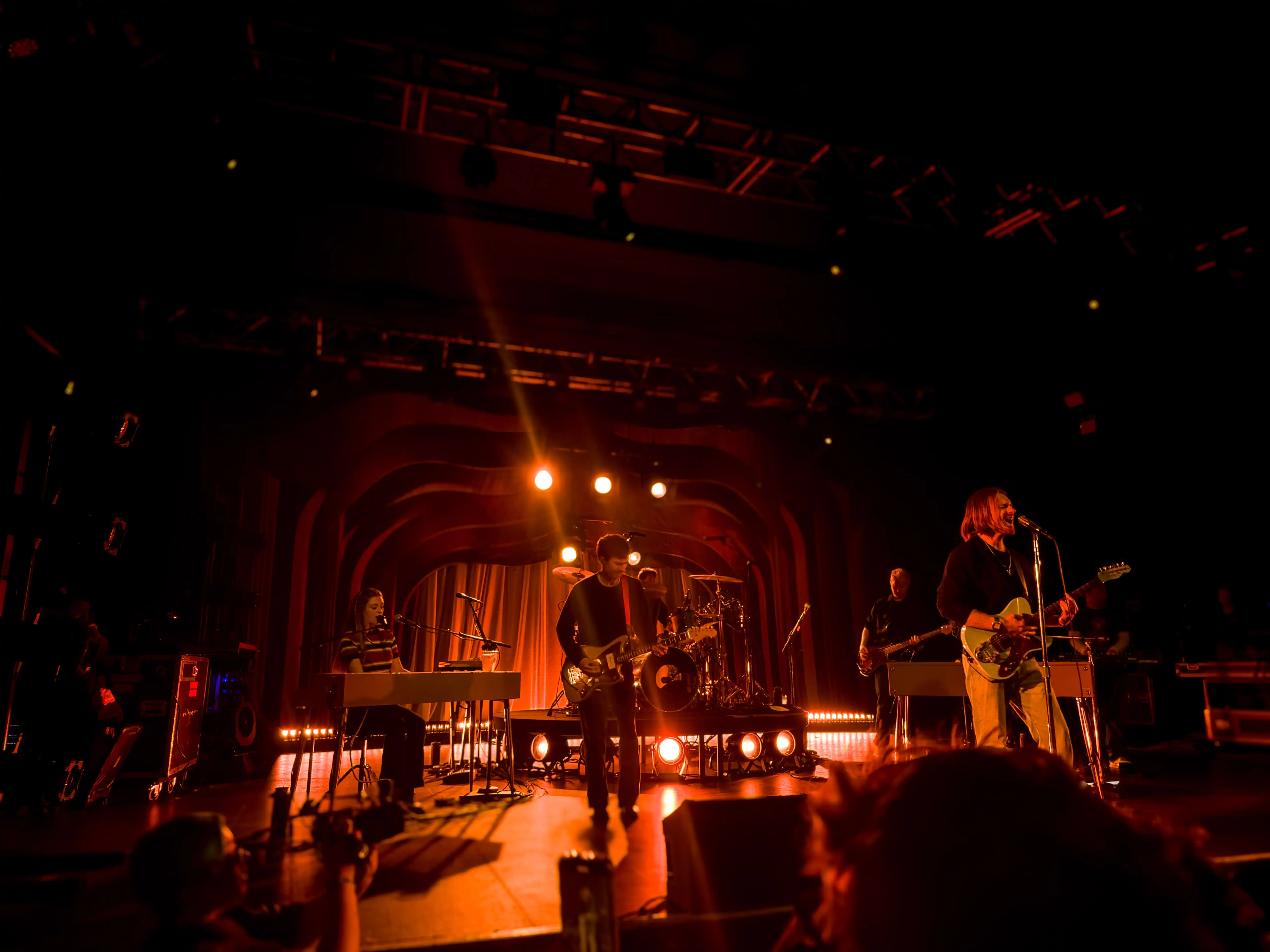 A dark and gloomy stage covered in a red stage light, on stage Finneas plays infront of a crowded audience.