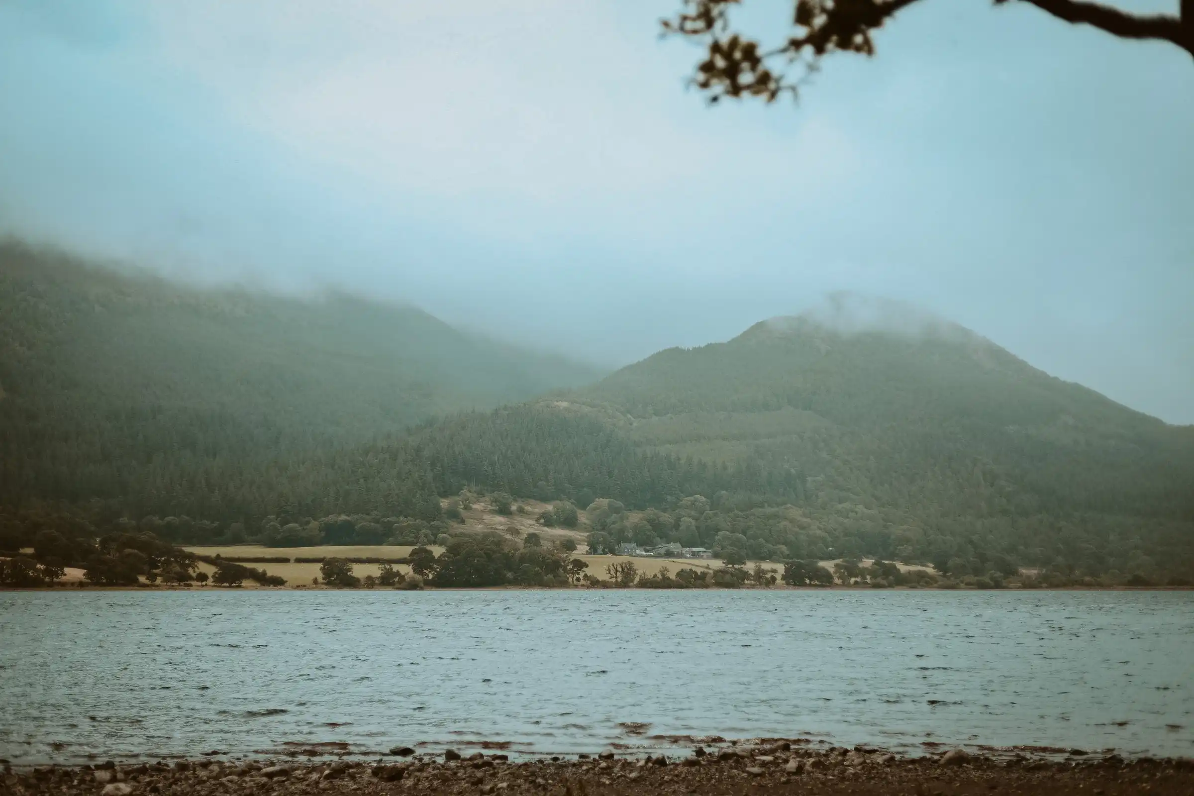 A distant shot of mountains covered by the clouds across a lake.