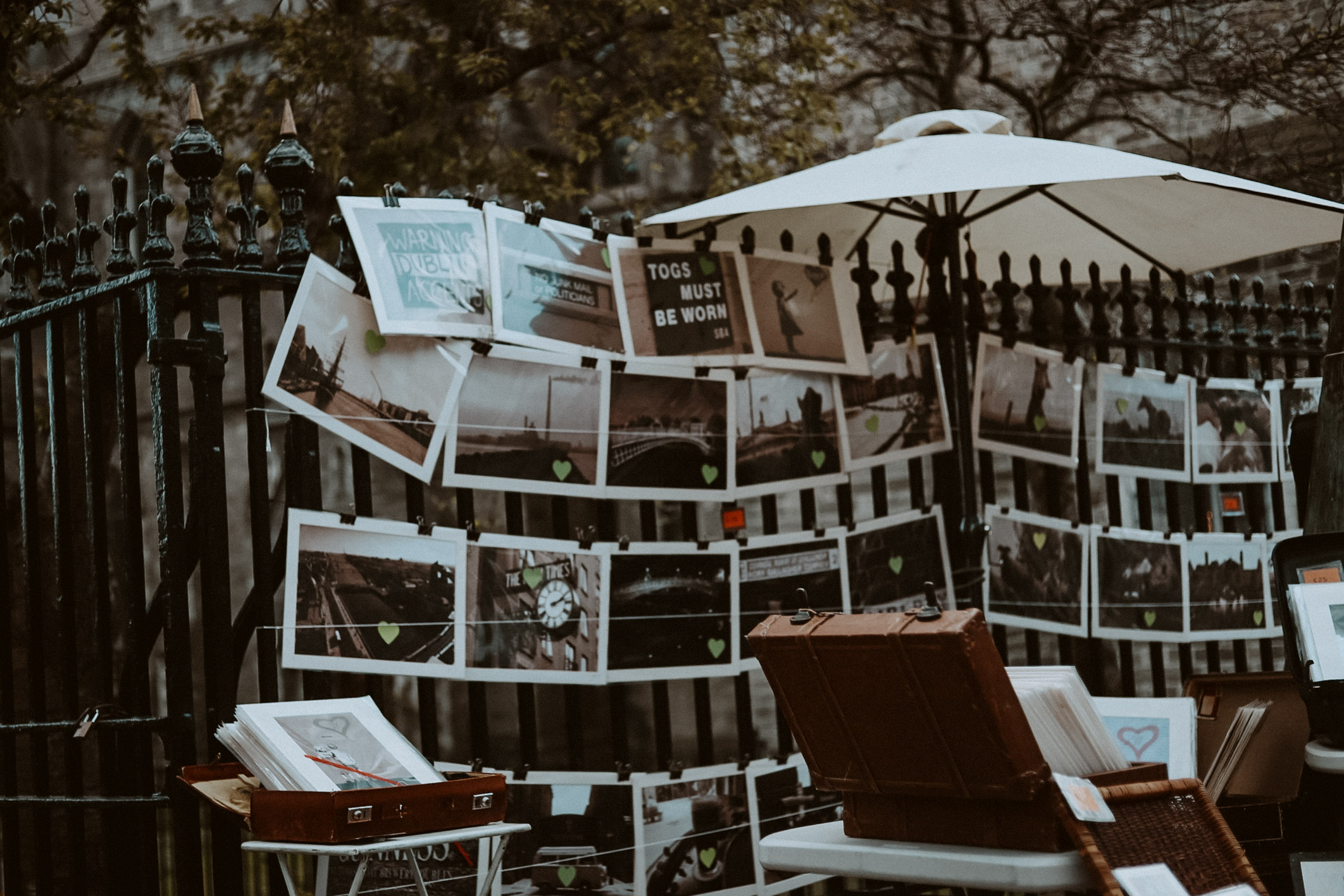 A string of printed images hung across a fence, there are four rows of these, all for sale from the vendor, bottom right is a vintage trunk assumingly what they were transported in.