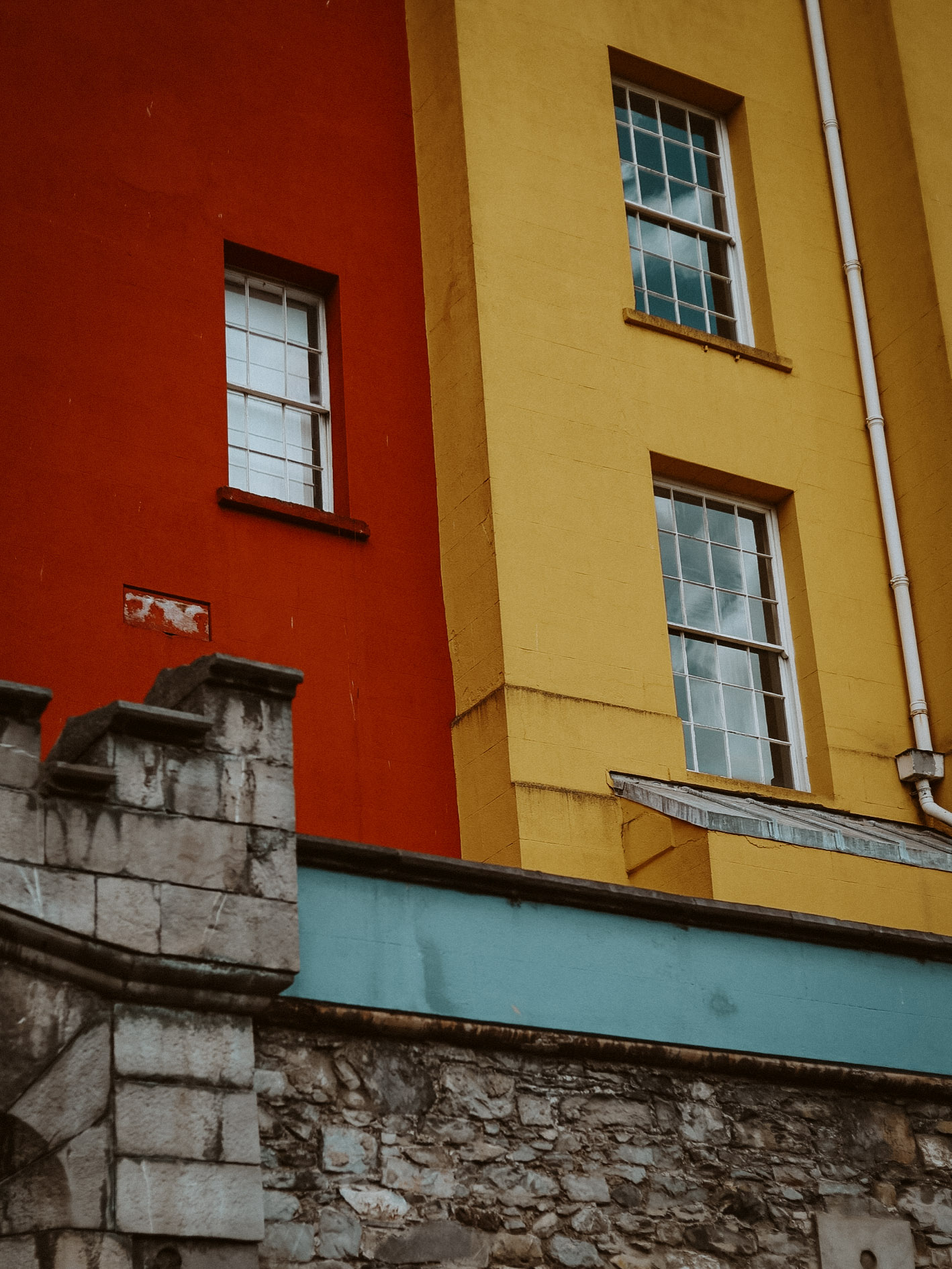Close up of three buildings, one vibrant red, one bright yellow parallel to each other, the least a surprisingly not dull gray connecting them across the bottom like a bridge.