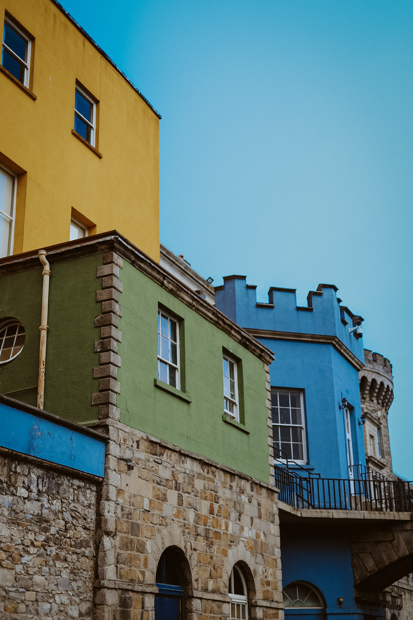 Similar to the second photo in which it is three buildings, one bright yellow, the next vibrant blue, the familiar surprisingly not dull grey plus an additional muted green to complement them all as wella s the architecture.